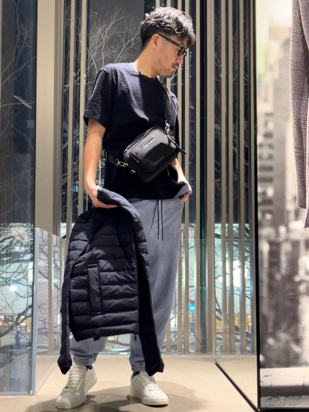 ブラック系のダウンジャケット/コート、ホワイト系のスニーカー、ブラック系のショルダーバッグを着用したメンズの春コーディネートの2枚目の写真