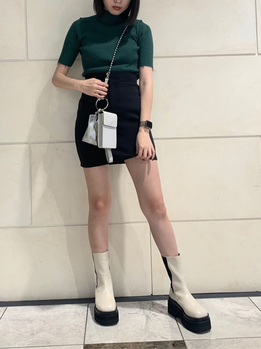 ブラック系のスカート、ホワイト系のハンドバッグ、グリーン系のニット/セーターを着用したレディースの夏コーディネートの2枚目の写真