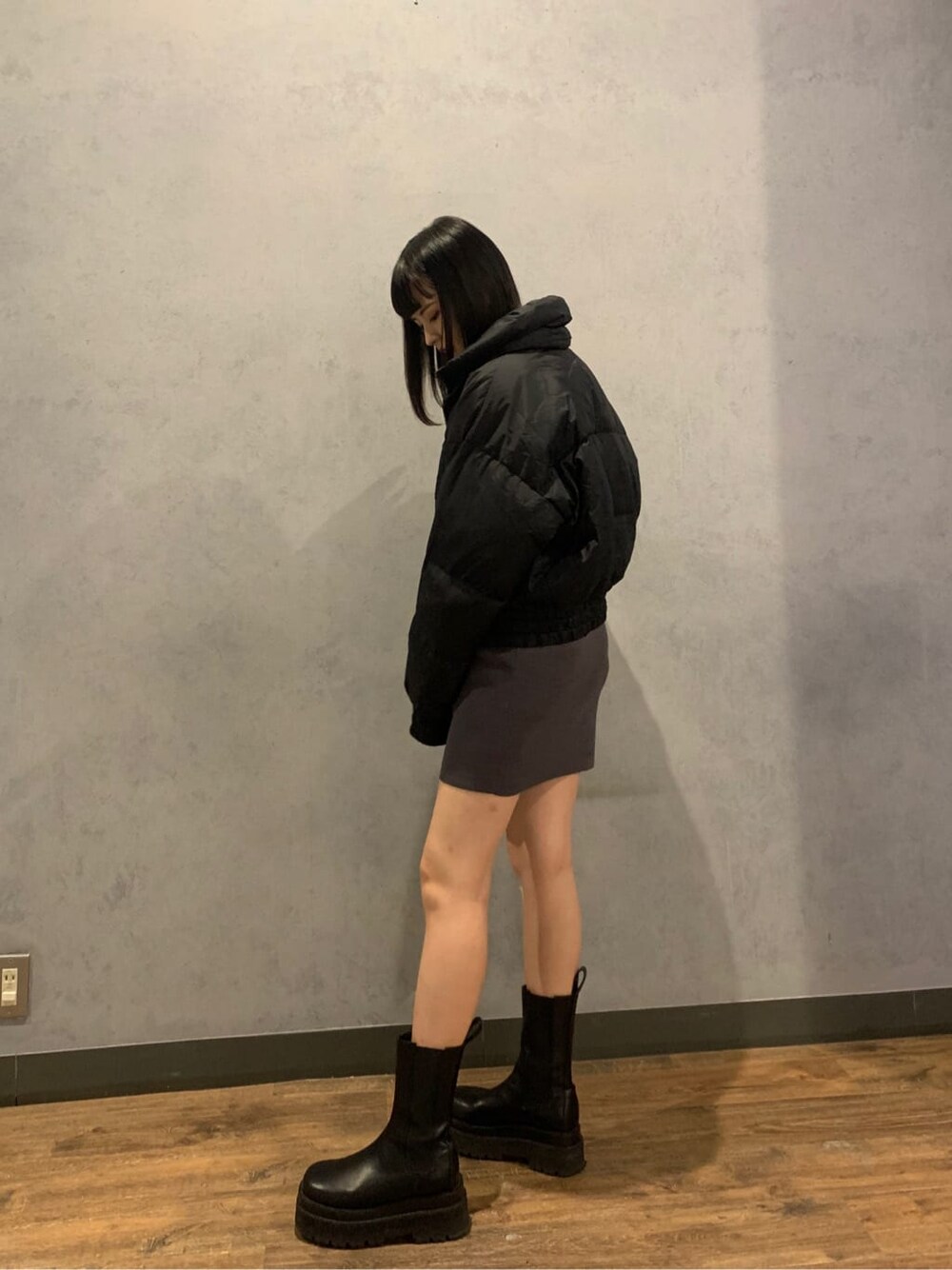 グレー系のワンピース、ブラック系のダウンジャケット/コート、ブラック系のブーツを着用したレディースの冬コーディネートの2枚目の写真