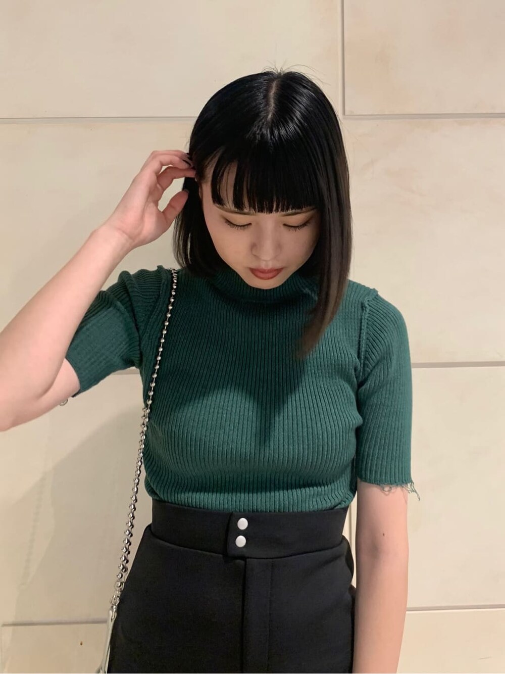 ブラック系のスカート、ホワイト系のハンドバッグ、グリーン系のニット/セーターを着用したレディースの夏コーディネートの3枚目の写真