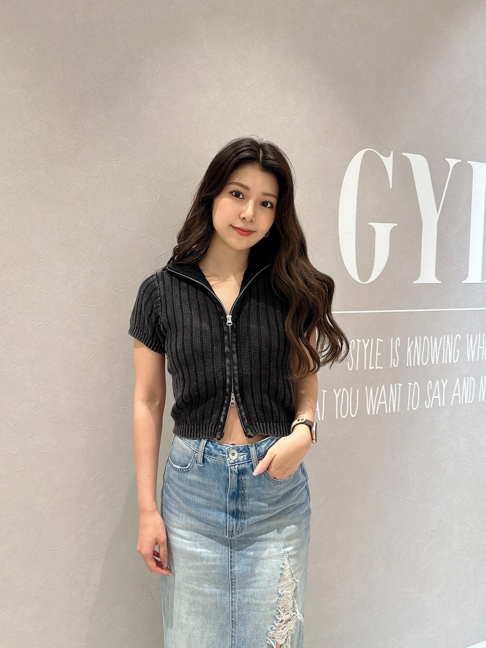 ブルー系のデニムスカート、ホワイト系のサンダル、ブラック系のニット/セーターを着用したレディースの夏コーディネートの4枚目の写真