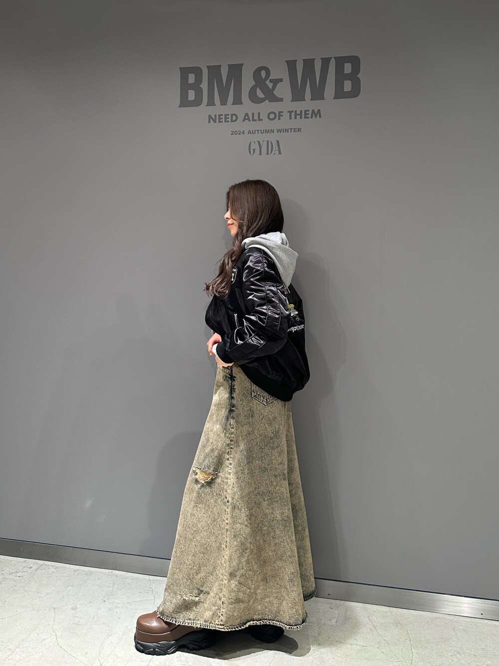 グレー系のパーカー、ブルー系のデニムスカート、ブラック系のブルゾンを着用したレディースの秋コーディネートの2枚目の写真