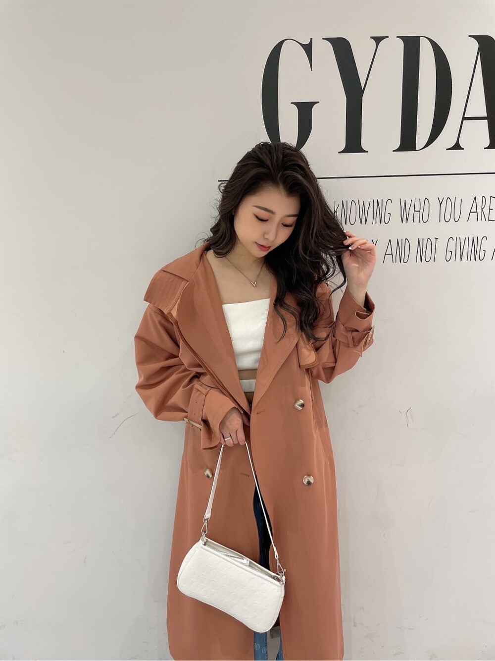 ホワイト系のキャミソール、ホワイト系のパンプス、オレンジ系のトレンチコートを着用したレディースの春コーディネートの4枚目の写真