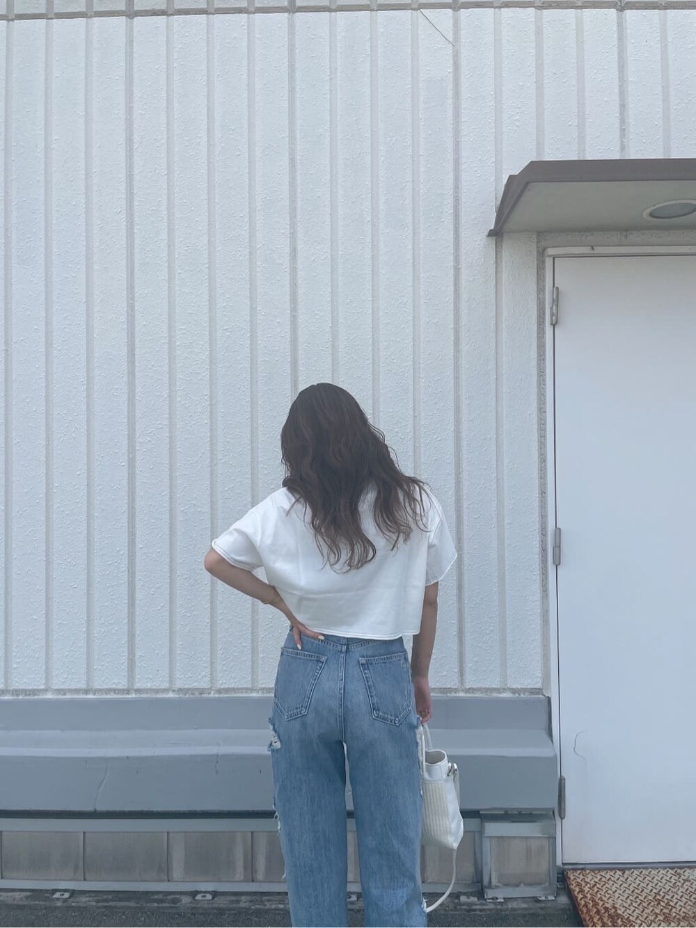 ホワイト系のハンドバッグ、ホワイト系のサンダル、ブルー系のデニムパンツを着用したレディースの夏コーディネートの5枚目の写真