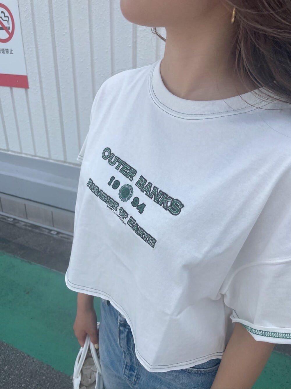 ホワイト系のハンドバッグ、ホワイト系のサンダル、ブルー系のデニムパンツを着用したレディースの夏コーディネートの8枚目の写真