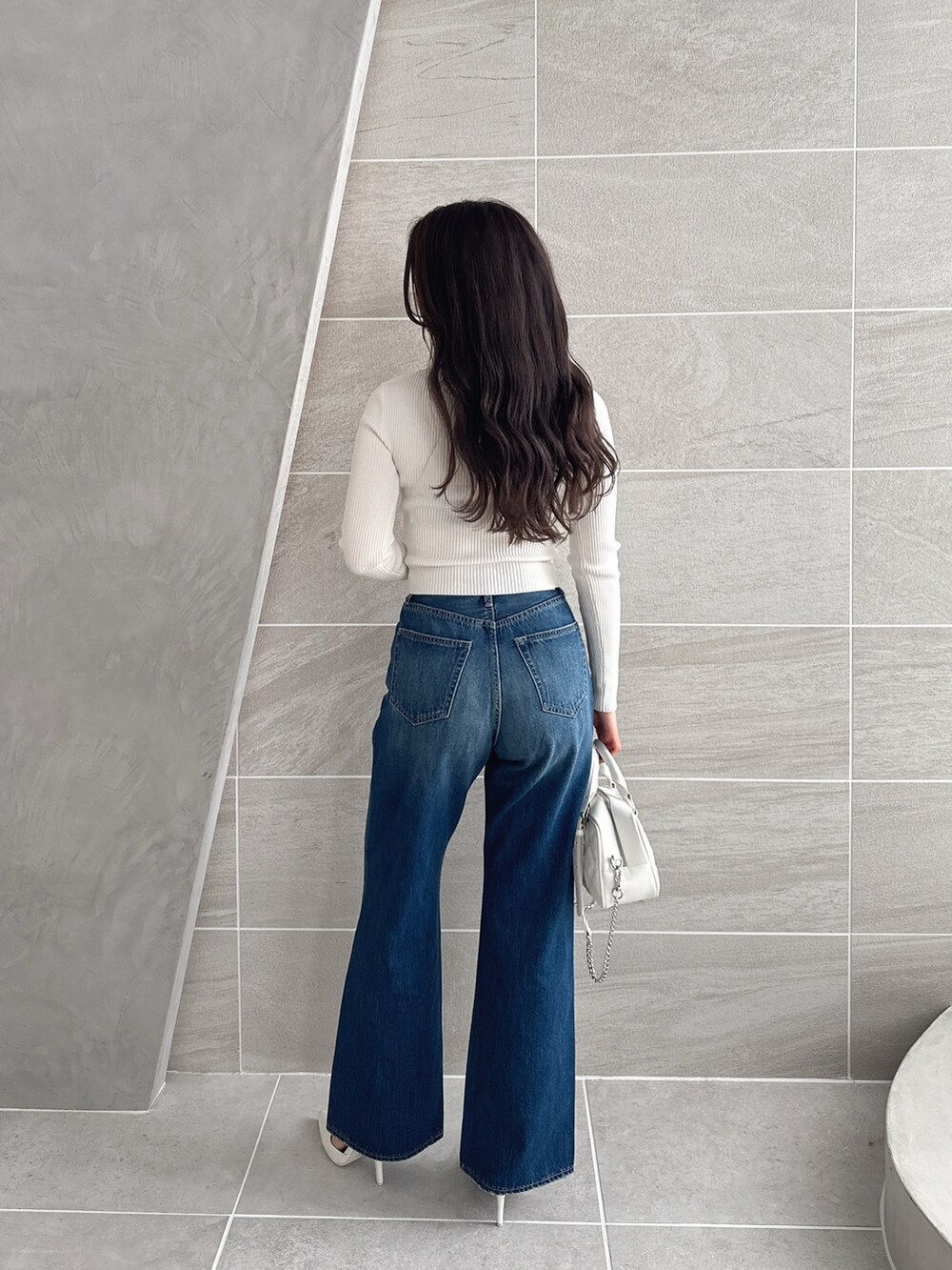 ブルー系のデニムパンツ、ホワイト系のパンプス、ホワイト系のハンドバッグを着用したレディースの冬コーディネートの2枚目の写真