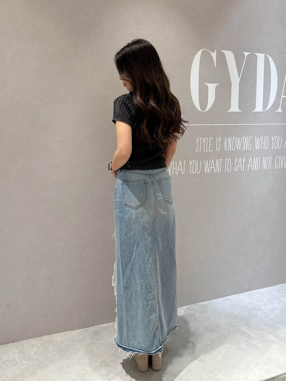 ブルー系のデニムスカート、ホワイト系のサンダル、ブラック系のニット/セーターを着用したレディースの夏コーディネートの3枚目の写真