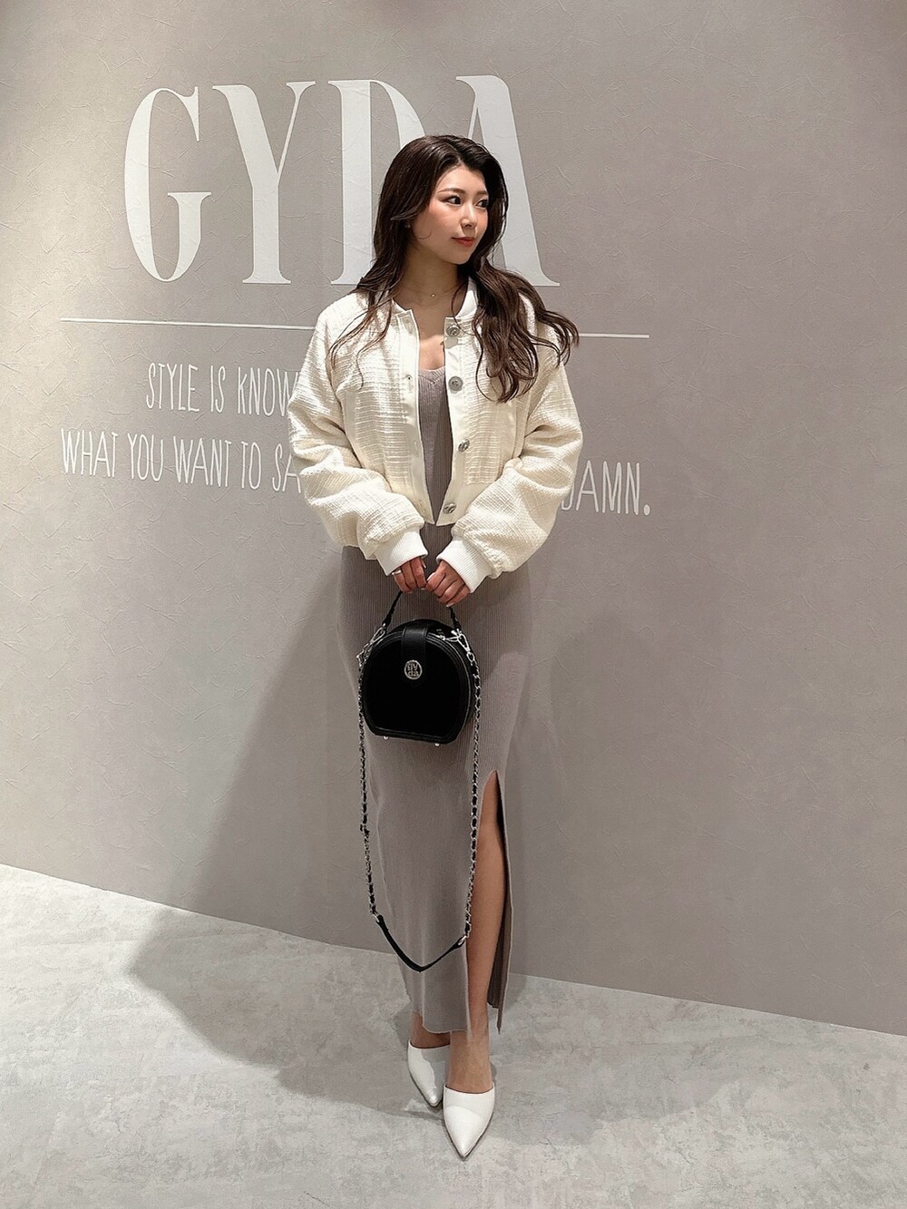 グレー系のワンピース、ホワイト系のブルゾン、ブラック系のハンドバッグを着用したレディースの春コーディネートの2枚目の写真