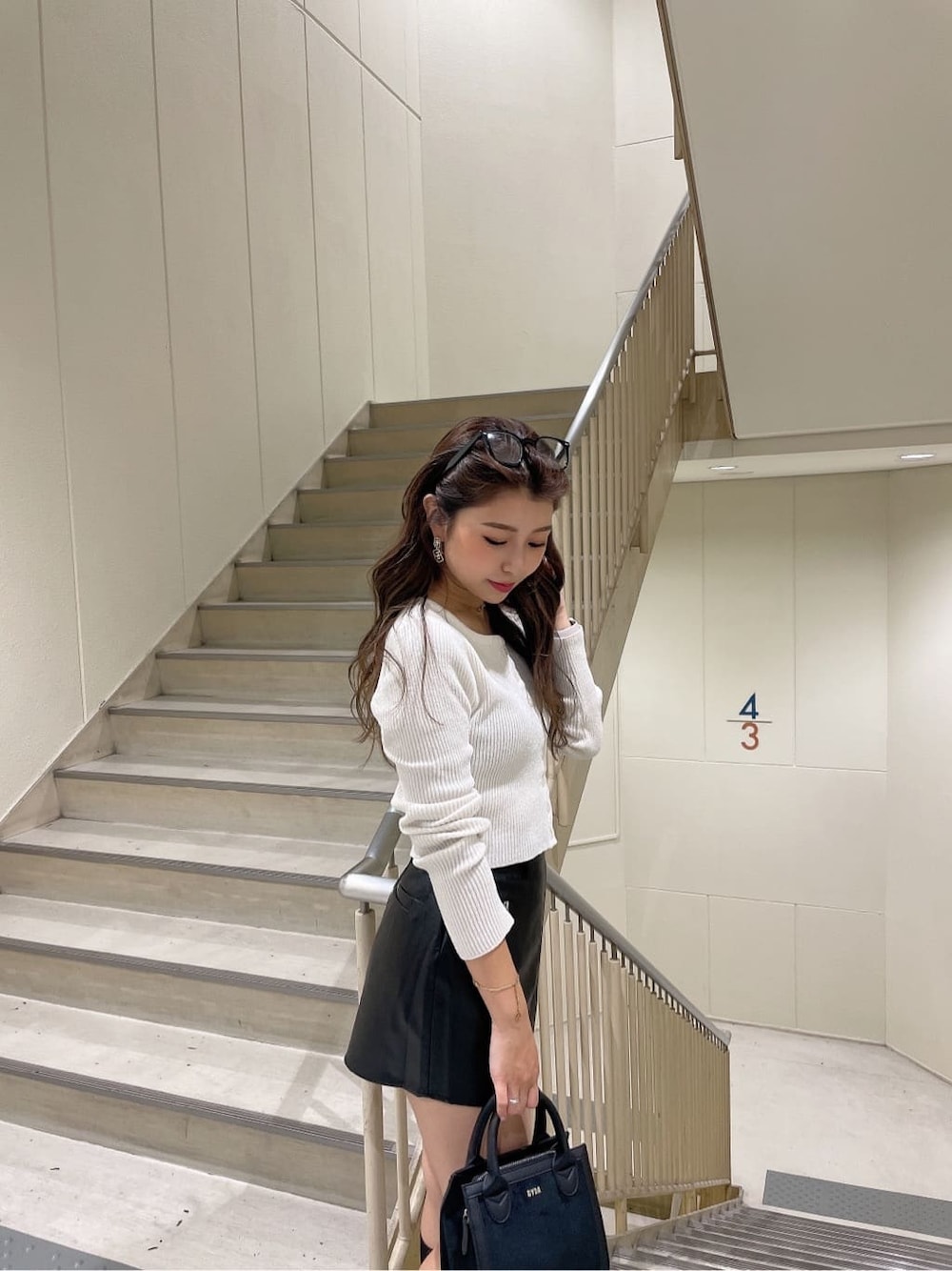 ブラック系のハンドバッグ、ブラック系のスカート、ホワイト系のカーディガン/ボレロを着用したレディースの秋コーディネートの6枚目の写真