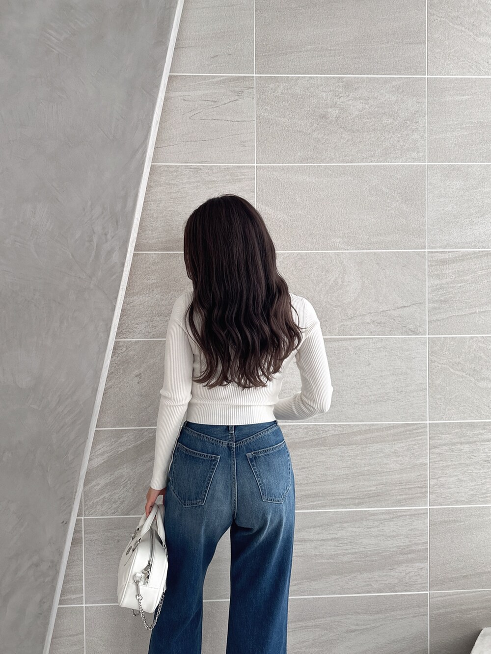 ブルー系のデニムパンツ、ホワイト系のパンプス、ホワイト系のハンドバッグを着用したレディースの冬コーディネートの5枚目の写真