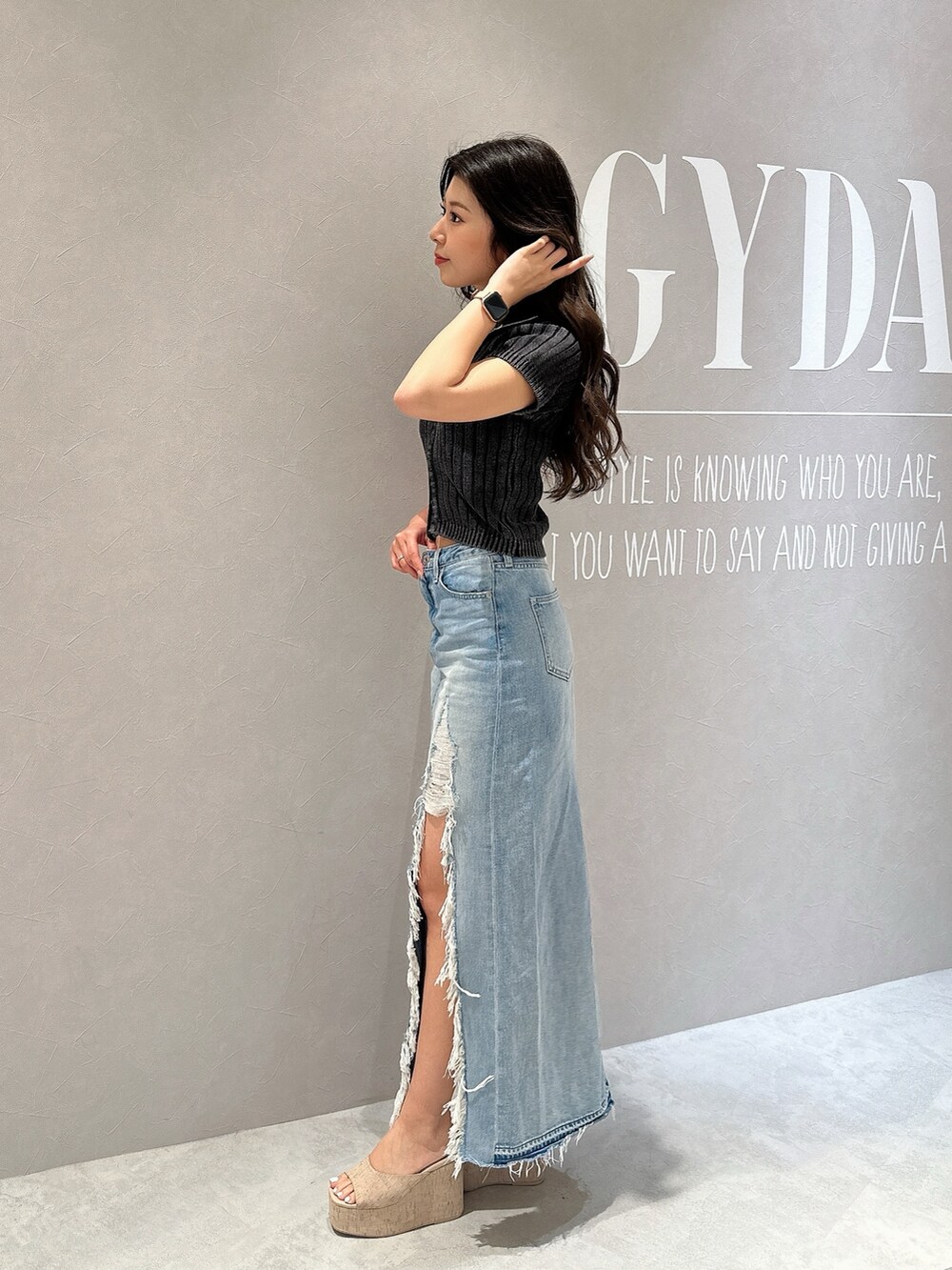 ブルー系のデニムスカート、ホワイト系のサンダル、ブラック系のニット/セーターを着用したレディースの夏コーディネートの2枚目の写真