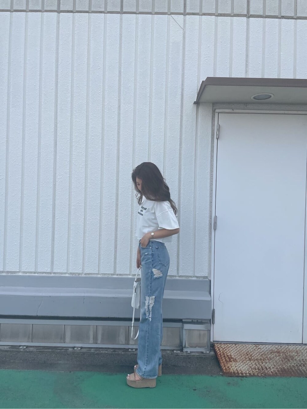 ホワイト系のハンドバッグ、ホワイト系のサンダル、ブルー系のデニムパンツを着用したレディースの夏コーディネートの3枚目の写真