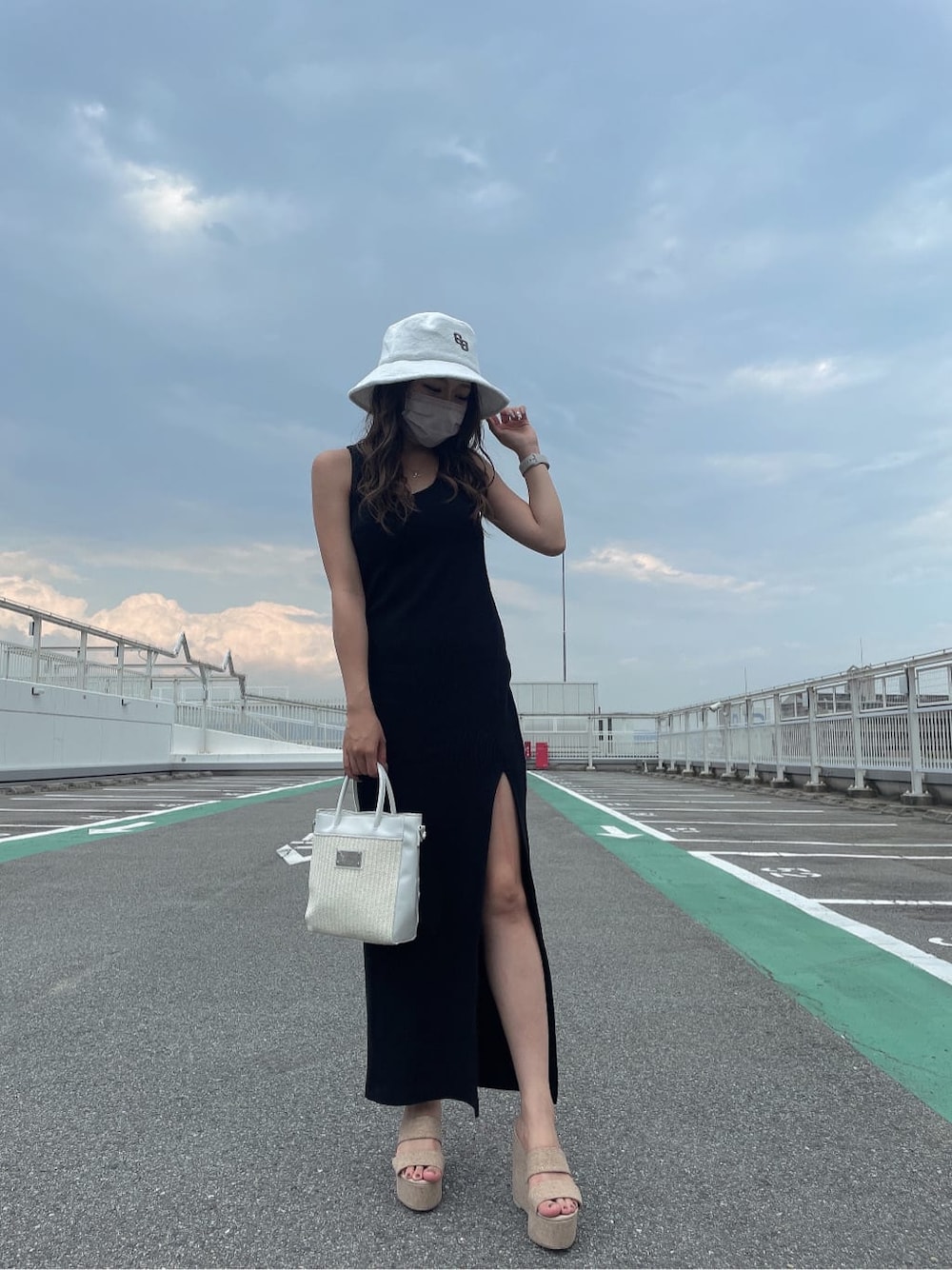 ホワイト系のサンダル、ホワイト系のハンドバッグ、ブラック系のワンピースを着用したレディースの夏コーディネートの3枚目の写真