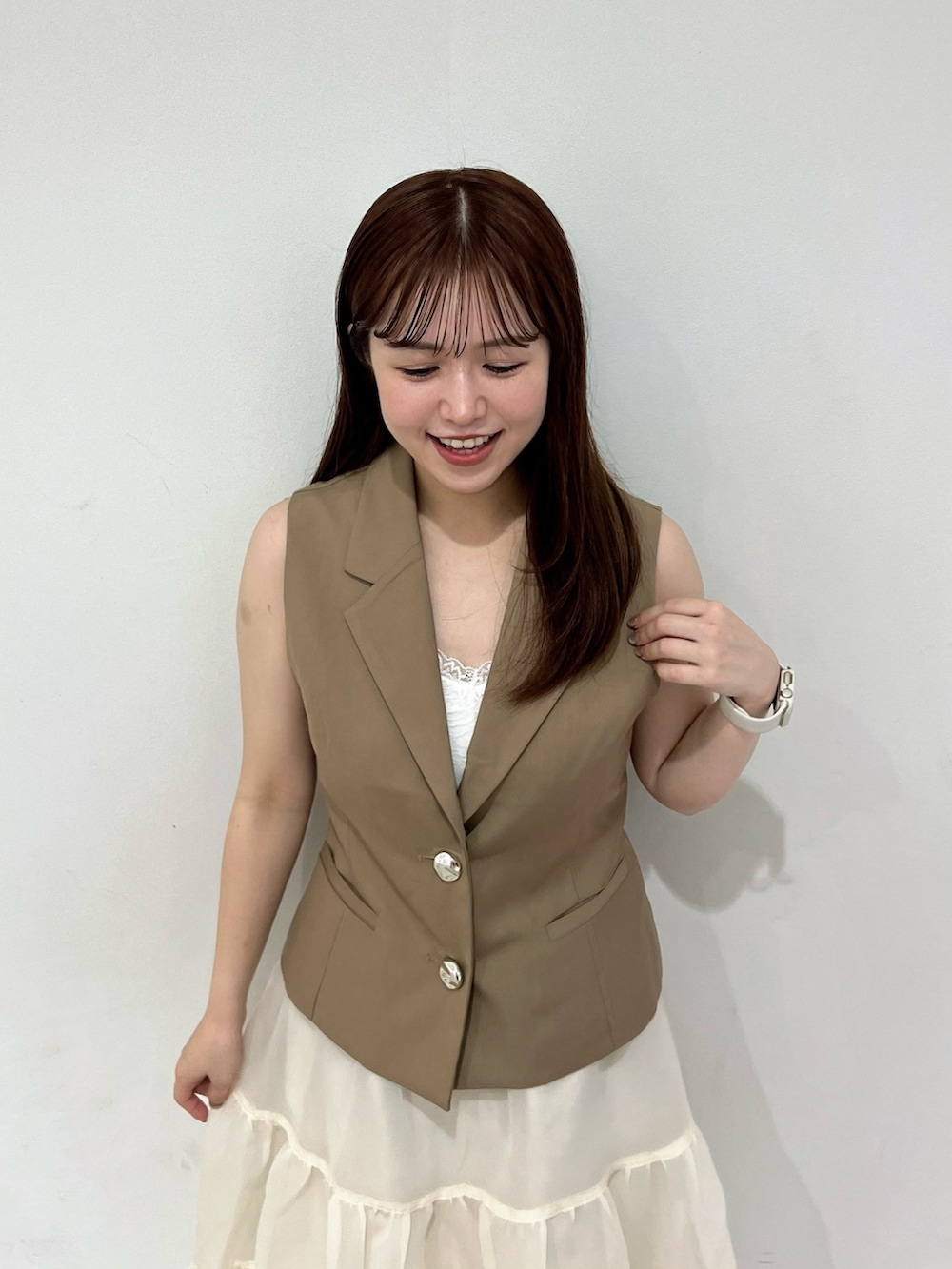 イエロー系のベスト、ベージュ系のスカート、ブラウン系のローファーを着用したレディースの夏コーディネートの3枚目の写真