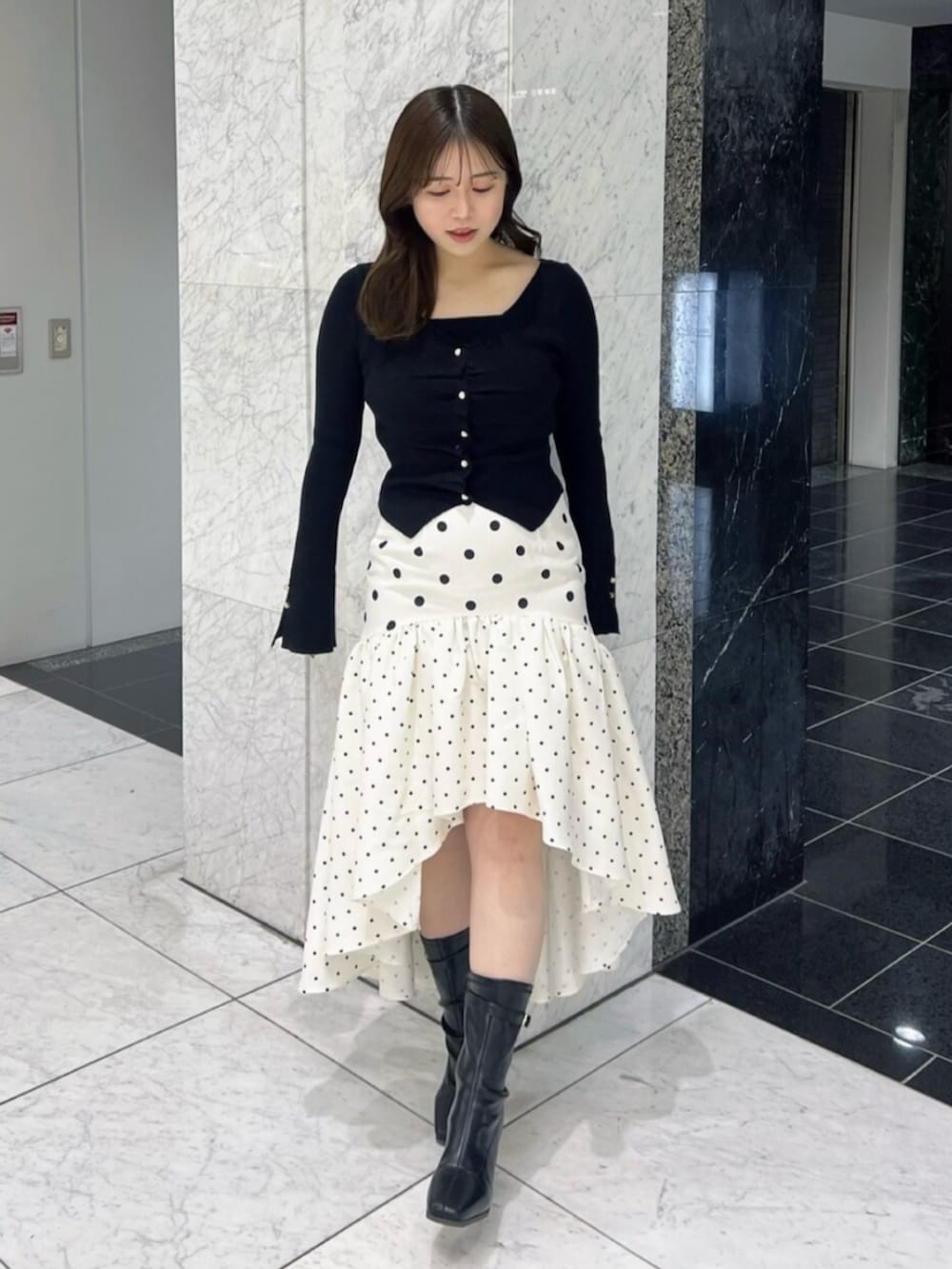 ブラック系のブーツ、ブラック系のニット/セーター、ホワイト系のスカートを着用したレディースの春コーディネートの2枚目の写真