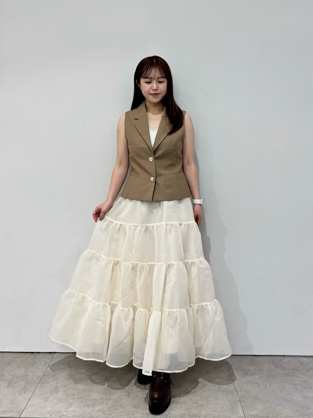 イエロー系のベスト、ベージュ系のスカート、ブラウン系のローファーを着用したレディースの夏コーディネートの2枚目の写真