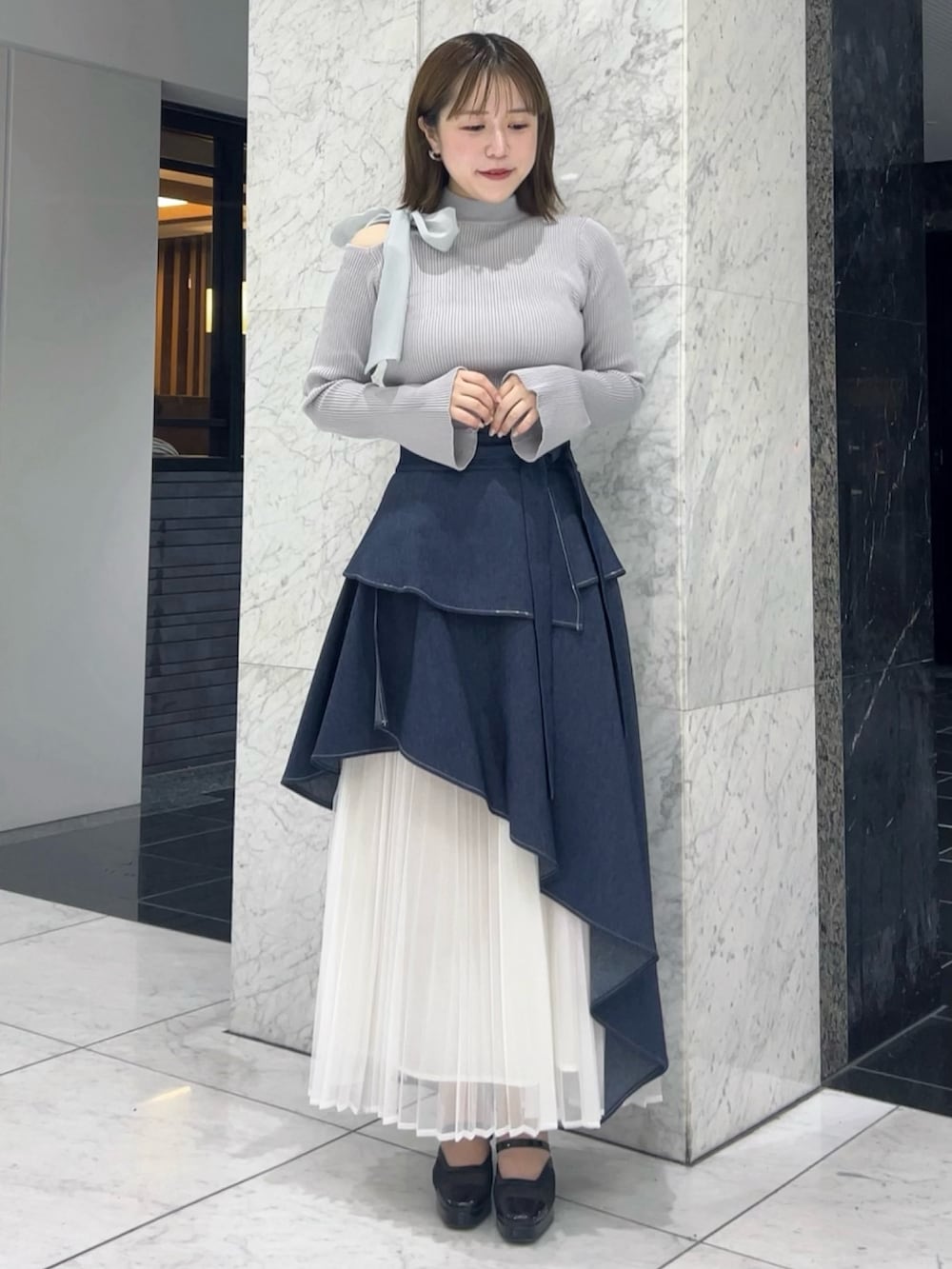 グレー系のニット/セーター、ブルー系のスカート、ブラック系のパンプスを着用したレディースの秋コーディネートの2枚目の写真