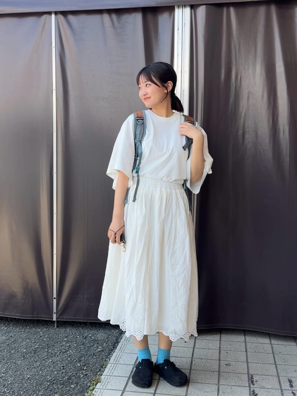 ブラック系のサンダル、ホワイト系のTシャツ/カットソー、ブラウン系のバックパック/リュックを着用したレディースの夏コーディネートの2枚目の写真