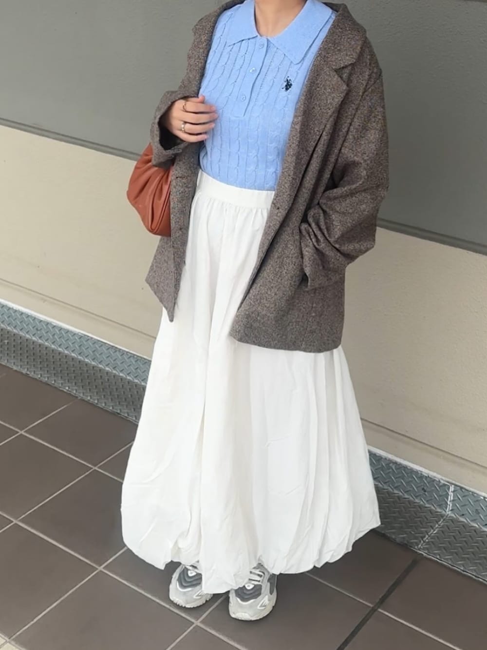 イエロー系のハンドバッグ、ベージュ系のスカート、ブラウン系のテーラードジャケットを着用したレディースの春コーディネートの2枚目の写真