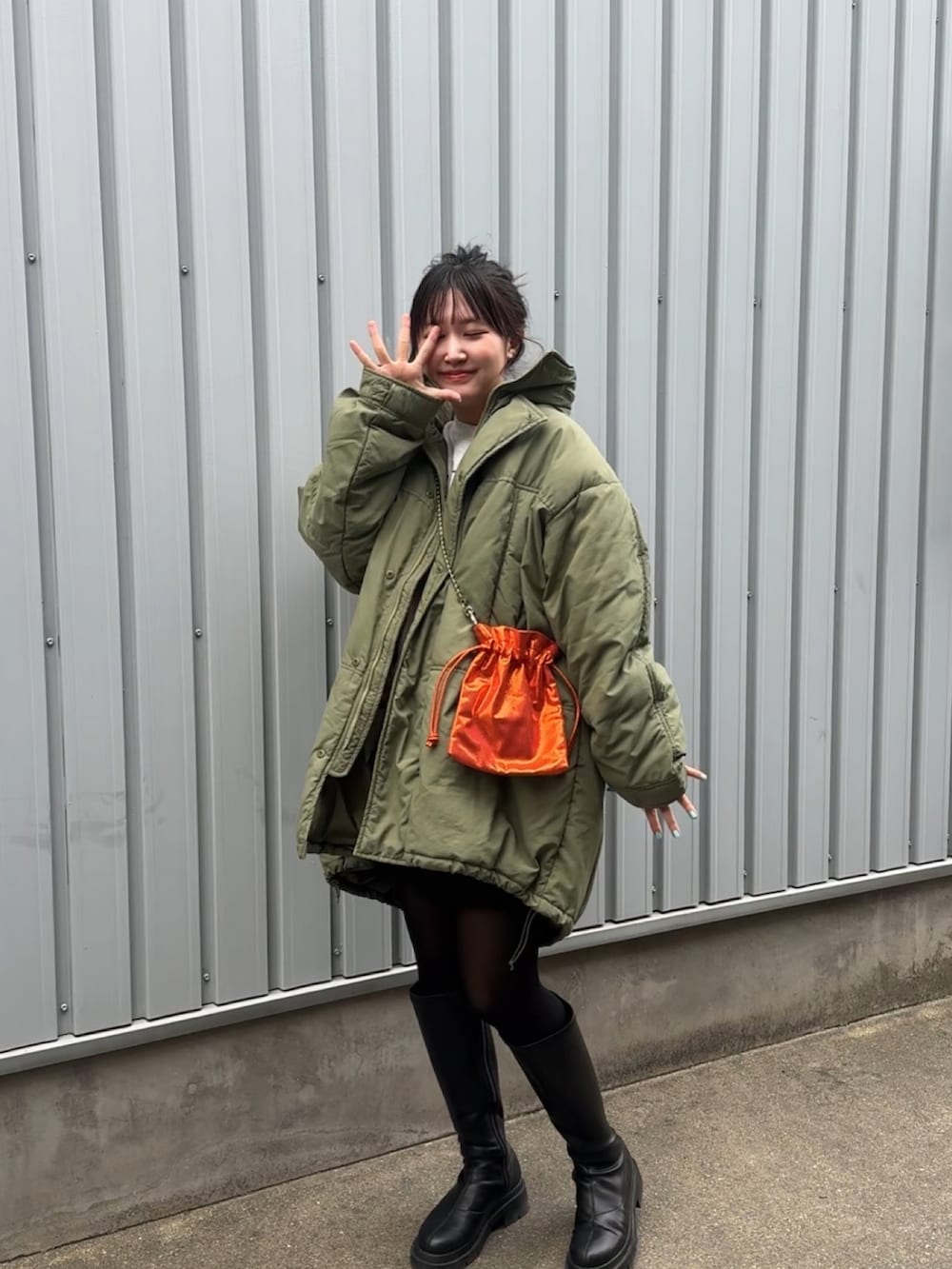 グリーン系のブルゾン、ブラック系のブーツ、オレンジ系のショルダーバッグを着用したレディースの冬コーディネートの3枚目の写真