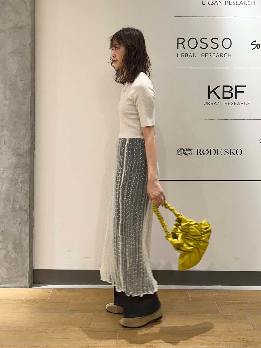 イエロー系のハンドバッグ、ホワイト系のスカート、ブルー系のデニムパンツを着用したレディースの秋コーディネートの4枚目の写真