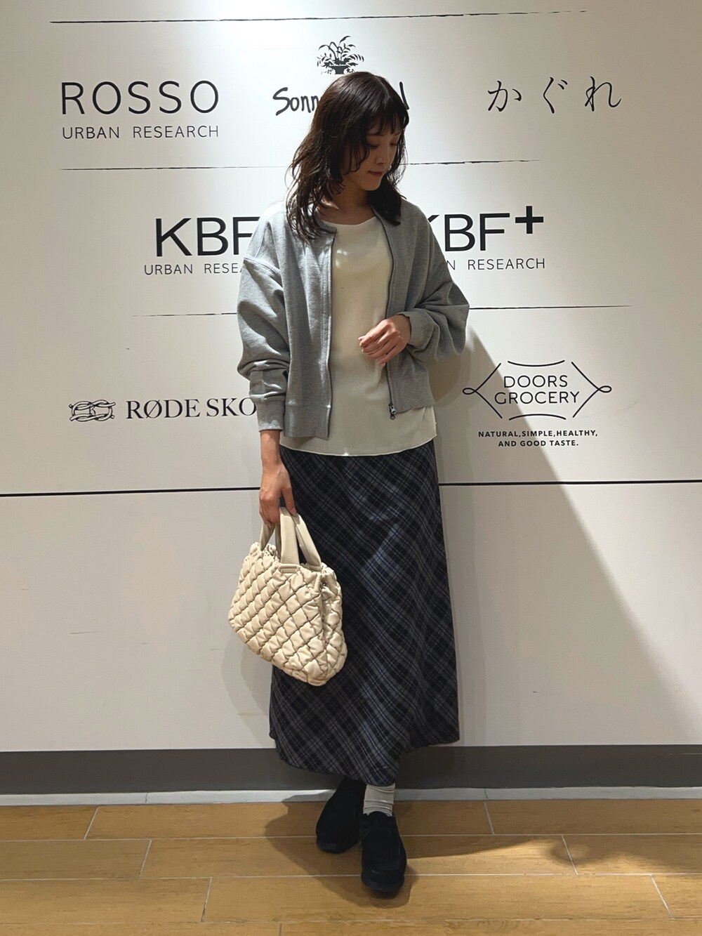 ホワイト系のハンドバッグ、ブルー系のスカート、ブラック系のブーツを着用したレディースの秋コーディネートの2枚目の写真