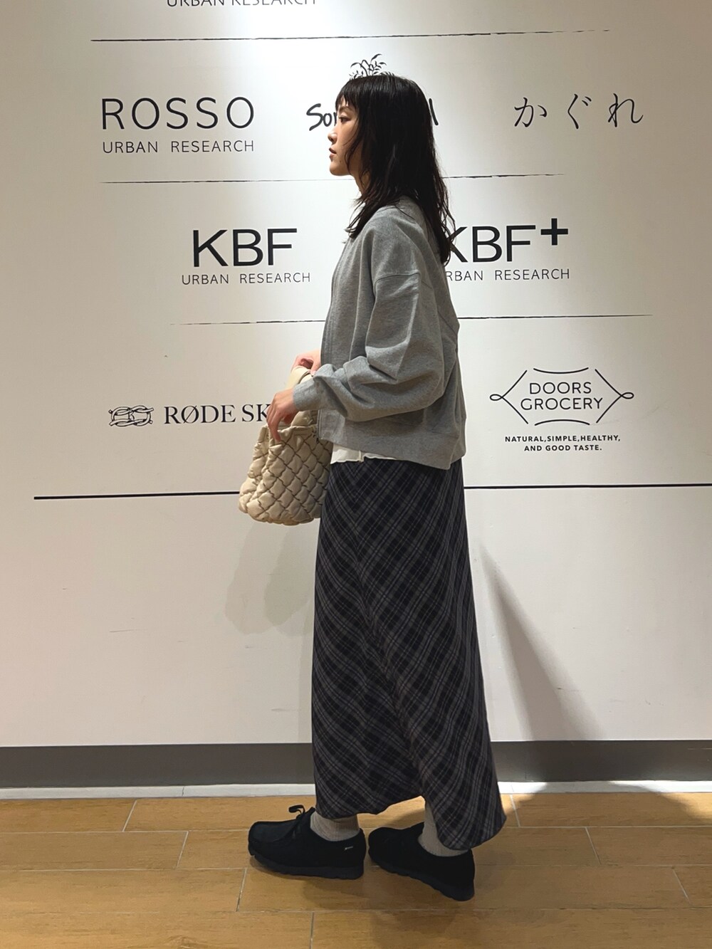 ホワイト系のハンドバッグ、ブルー系のスカート、ブラック系のブーツを着用したレディースの秋コーディネートの3枚目の写真