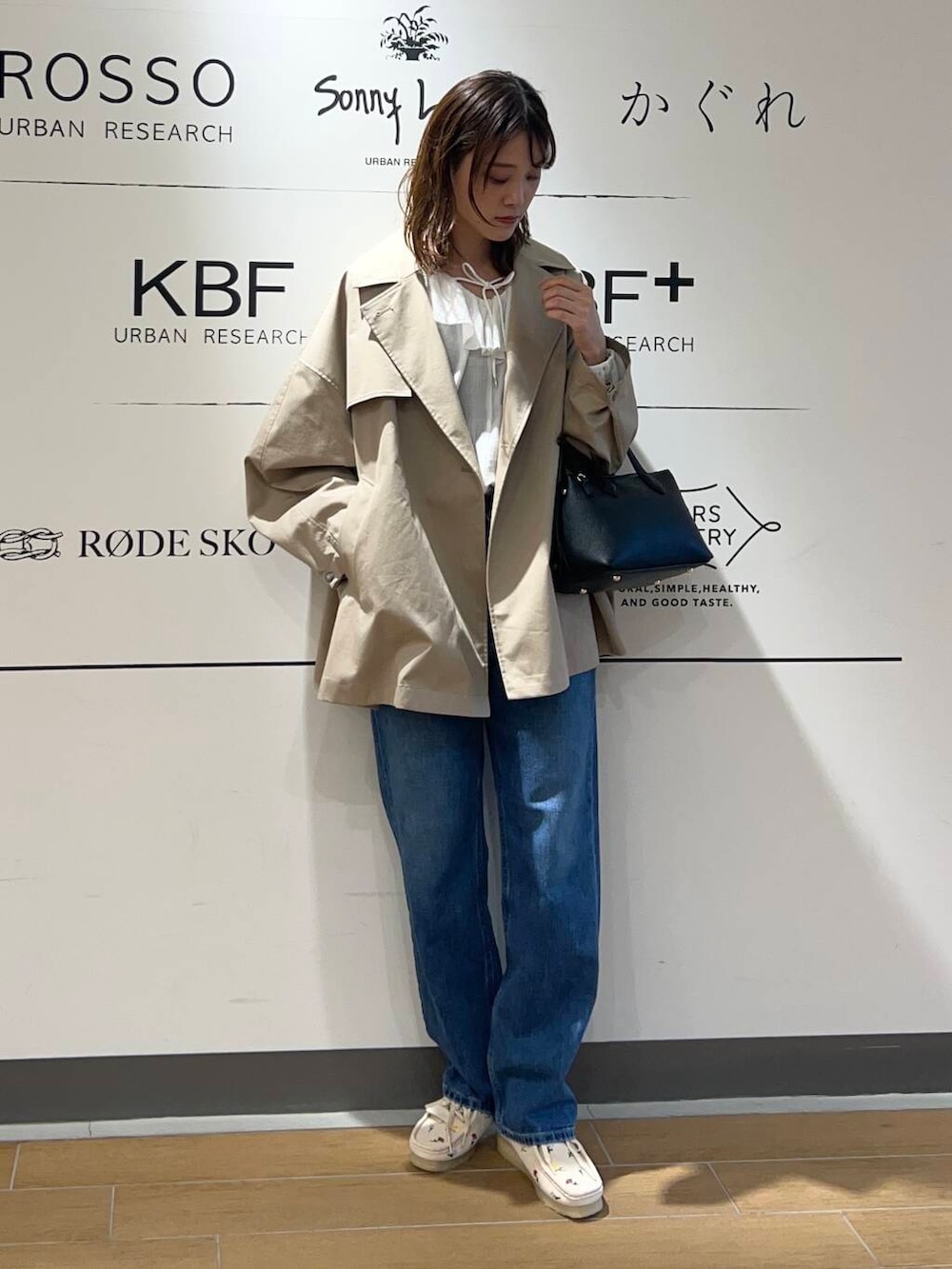 ベージュ系のトレンチコート、ブルー系のデニムパンツ、ブラック系のトートバッグを着用したレディースの春コーディネートの2枚目の写真