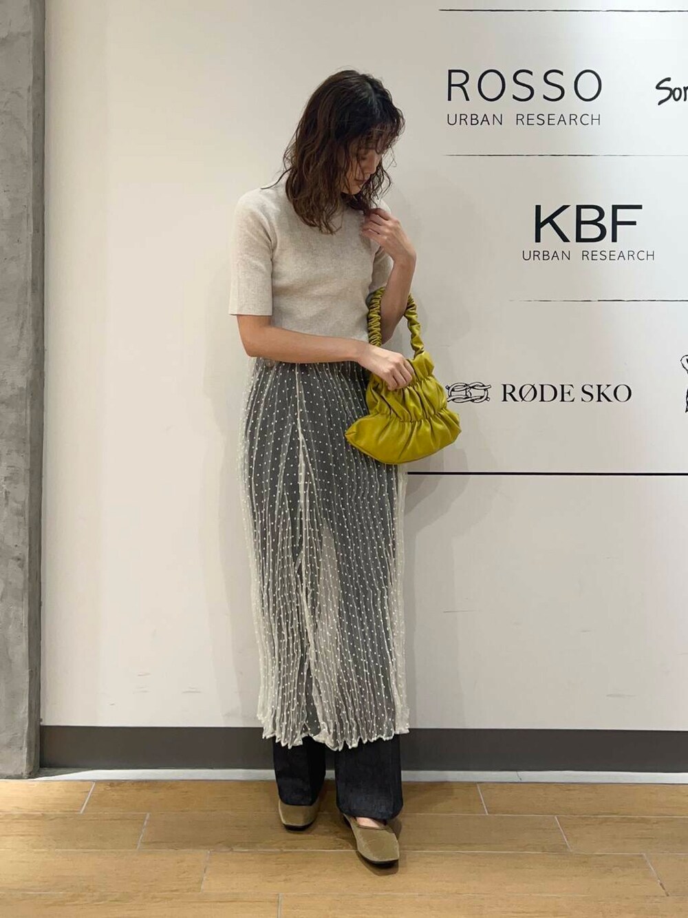 イエロー系のハンドバッグ、ホワイト系のスカート、ブルー系のデニムパンツを着用したレディースの秋コーディネートの3枚目の写真