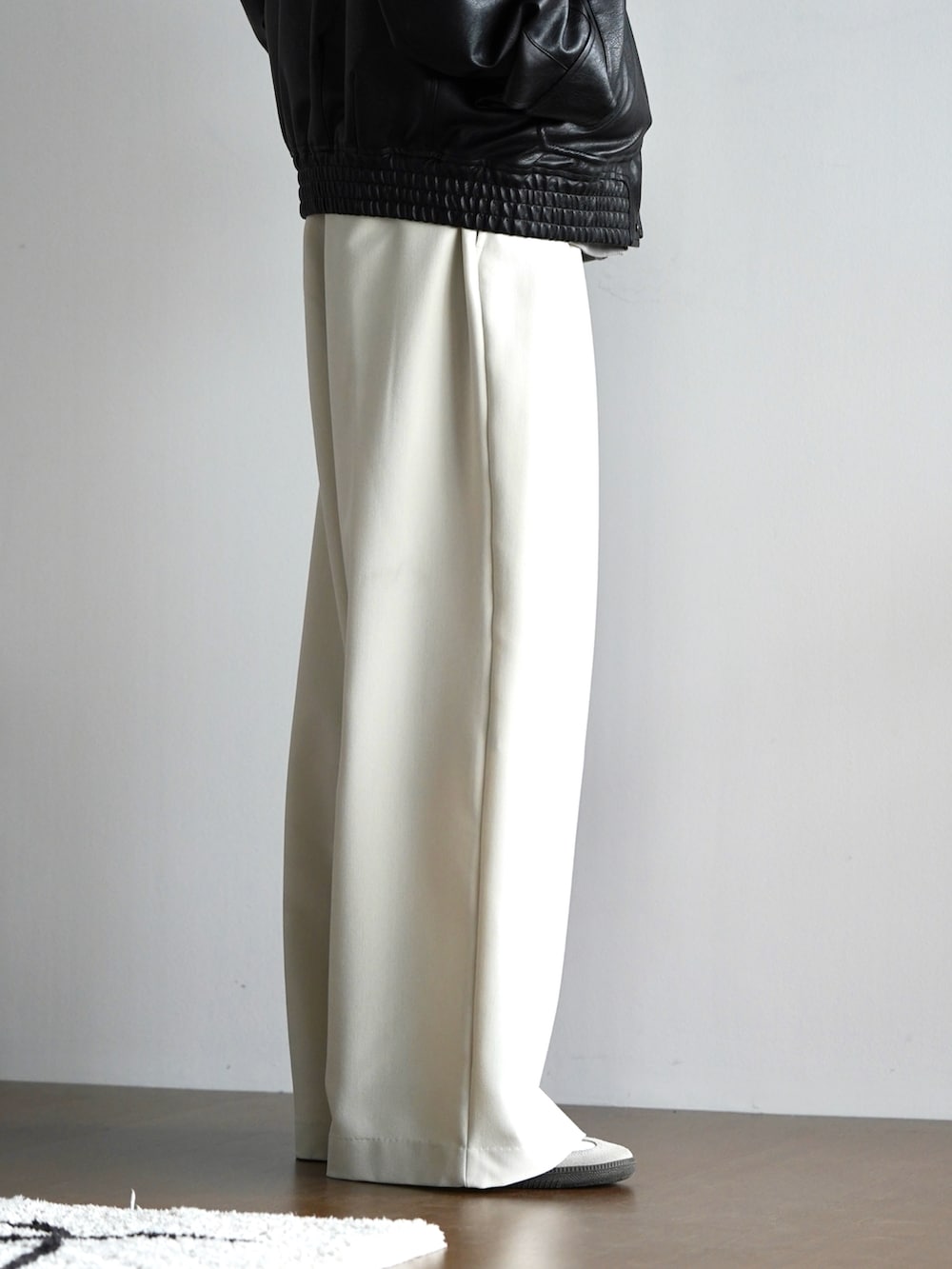 グレー系のパーカー、ブラック系のブルゾン、ホワイト系のスラックスを着用したメンズの秋コーディネートの4枚目の写真