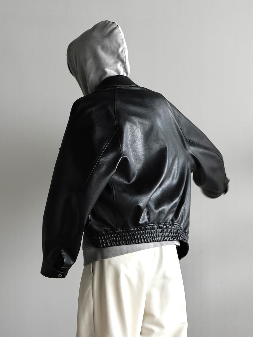 グレー系のパーカー、ブラック系のブルゾン、ホワイト系のスラックスを着用したメンズの秋コーディネートの5枚目の写真