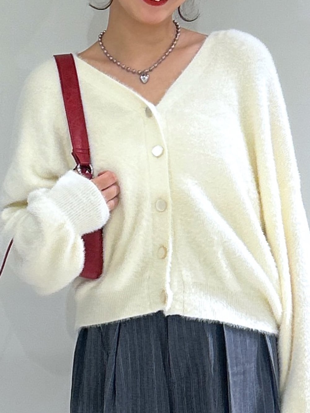 グレー系のスラックス、ホワイト系のニット/セーター、レッド系のショルダーバッグを着用したレディースの秋コーディネートの4枚目の写真