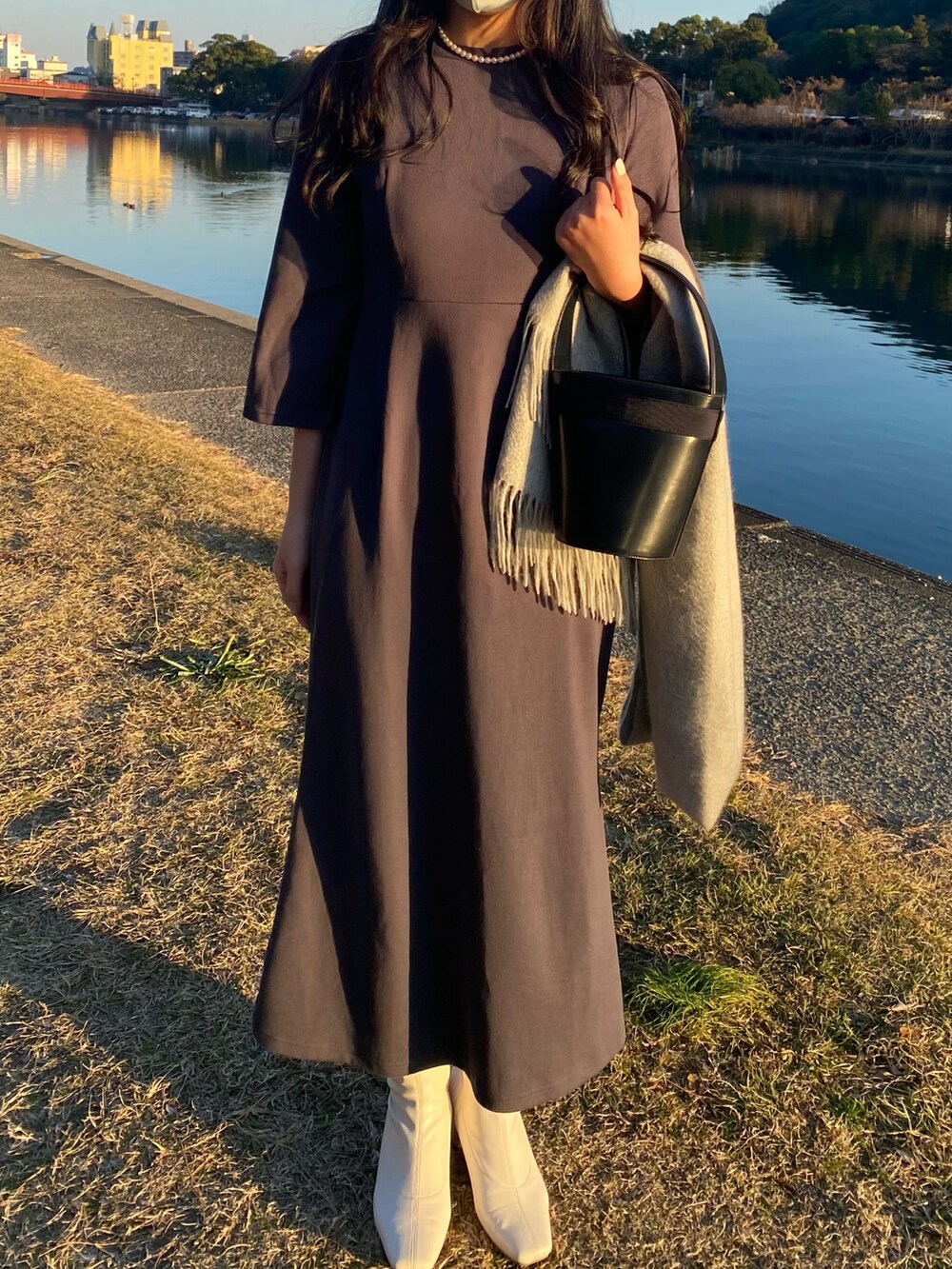 グレー系のワンピース、ホワイト系のブーツ、ブラック系のハンドバッグを着用したレディースの冬コーディネートの2枚目の写真