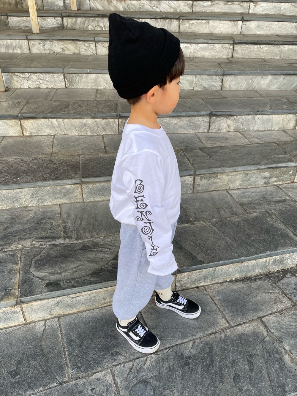 ホワイト系のTシャツ/カットソー、グレー系のスラックス、ブラック系のスニーカーを着用したキッズの秋コーディネートの2枚目の写真