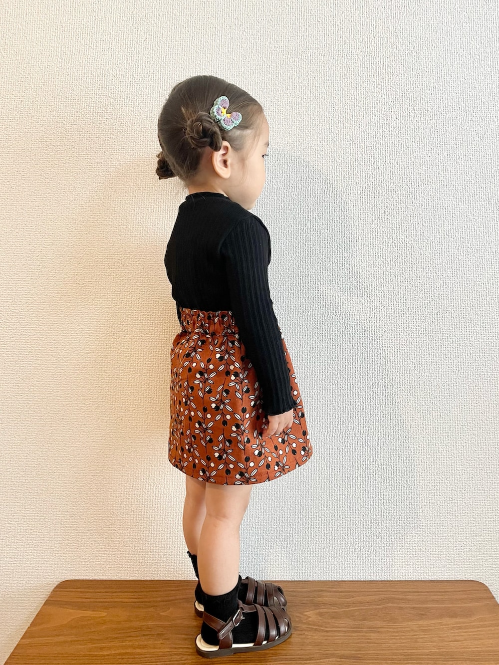 ブラック系のニット/セーター、オレンジ系のスカート、ブラウン系のサンダルを着用したキッズの秋コーディネートの2枚目の写真