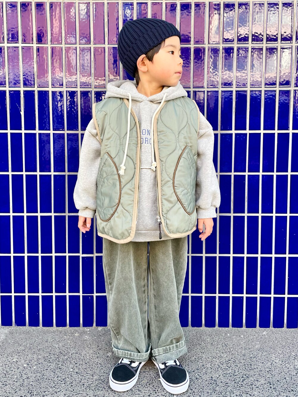 グレー系のパーカー、グリーン系のベスト、グリーン系のデニムパンツを着用したキッズの冬コーディネートの2枚目の写真