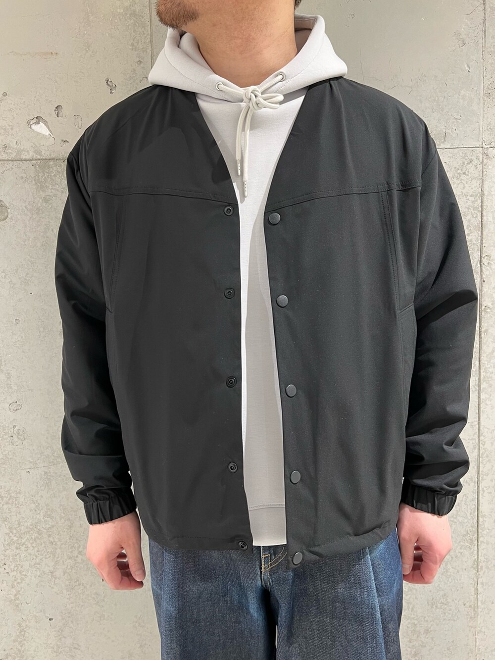 ブラック系のカーディガン/ボレロ、グレー系のパーカー、ブルー系のデニムパンツを着用したメンズの春コーディネートの4枚目の写真