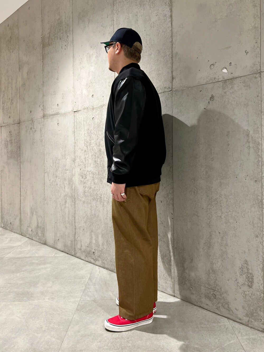 ブラック系のスタジャン、レッド系のスニーカー、ブラウン系のデニムパンツを着用したメンズの秋コーディネートの2枚目の写真