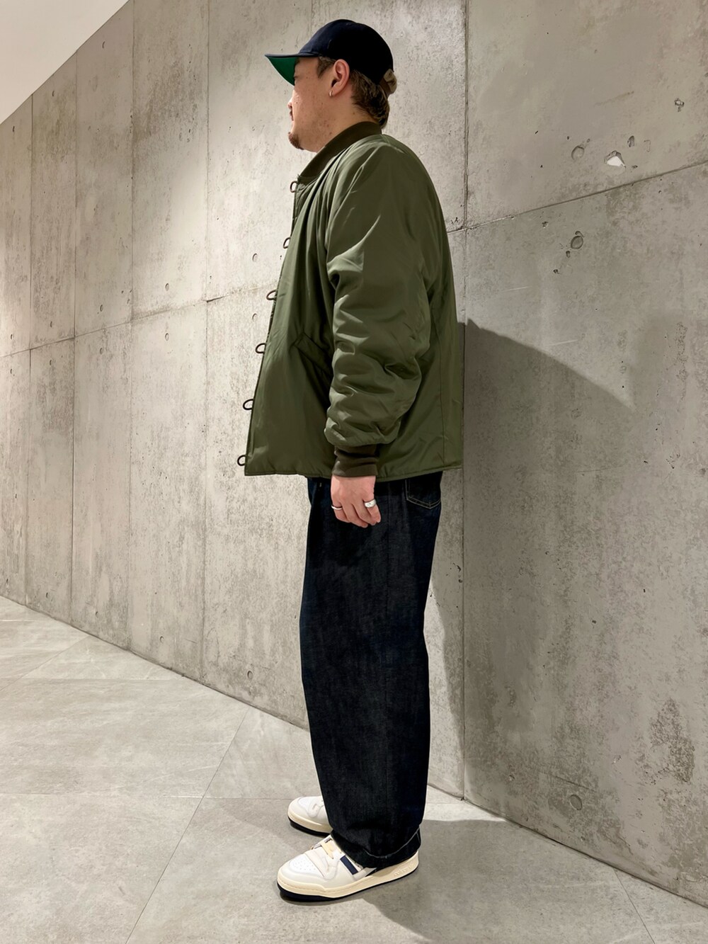 グリーン系のブルゾン、ブルー系のデニムパンツ、ホワイト系のスニーカーを着用したメンズの秋コーディネートの2枚目の写真
