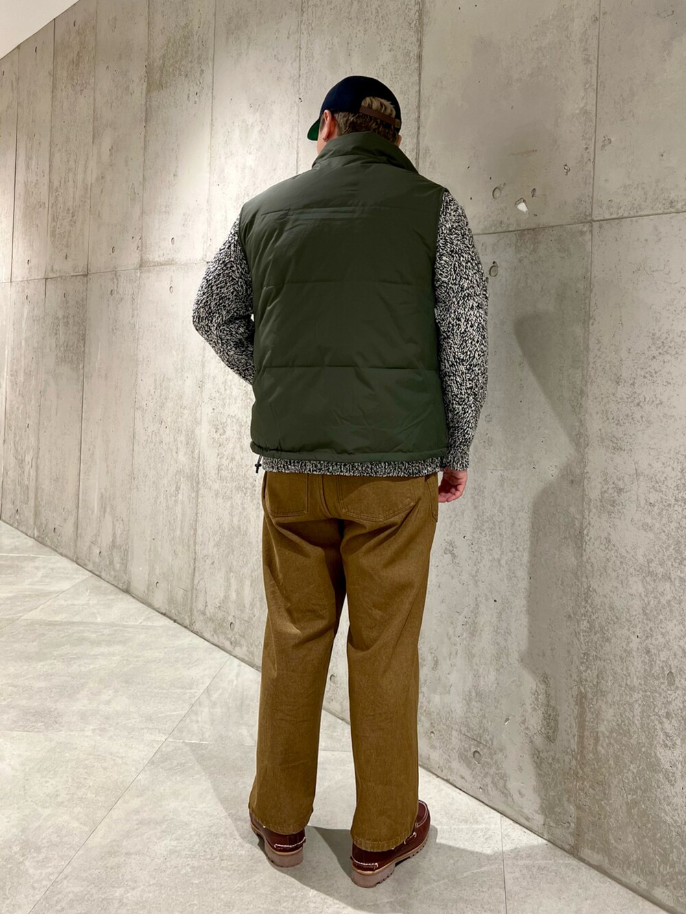 レッド系のモカシン/デッキシューズ、ブラウン系のデニムパンツ、グリーン系のダウンベストを着用したメンズの秋コーディネートの3枚目の写真