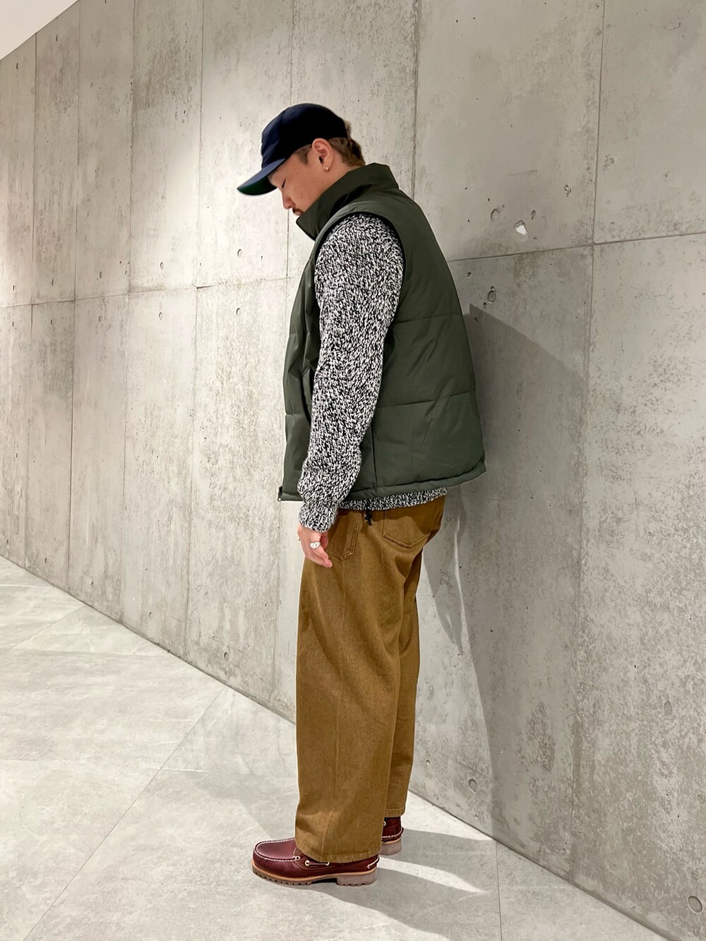 レッド系のモカシン/デッキシューズ、ブラウン系のデニムパンツ、グリーン系のダウンベストを着用したメンズの秋コーディネートの2枚目の写真