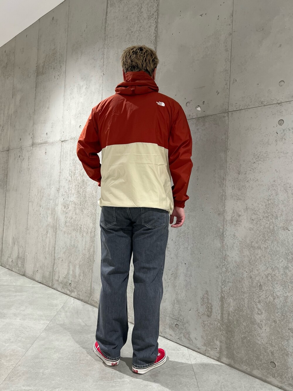 レッド系のナイロンジャケット、ブラック系のデニムパンツ、レッド系のスニーカーを着用したメンズの春コーディネートの3枚目の写真