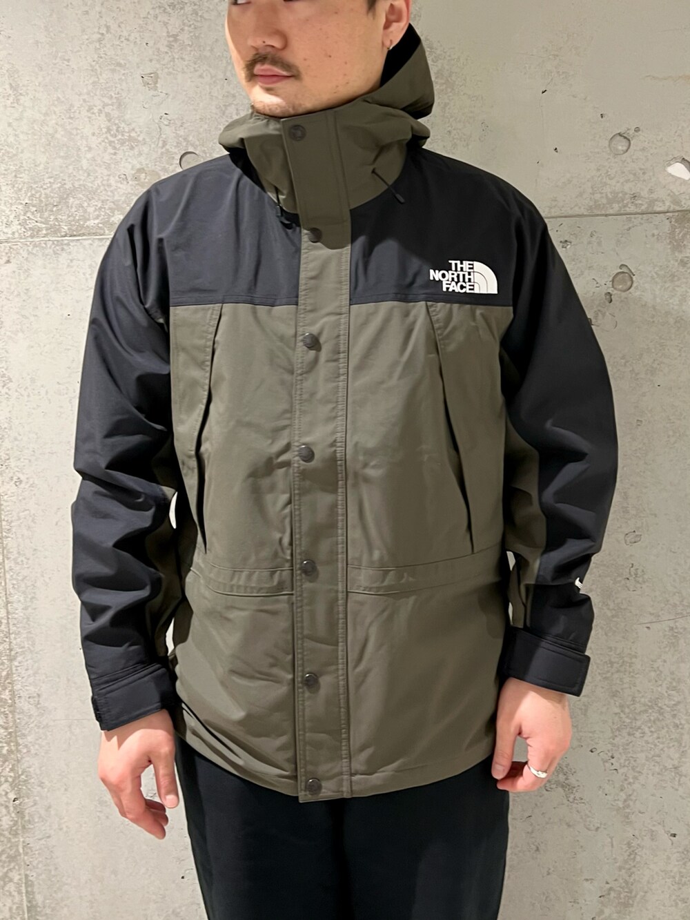 グリーン系のナイロンジャケット、ブラック系のスニーカー、ブラック系のスウェットパンツを着用したメンズの春コーディネートの2枚目の写真