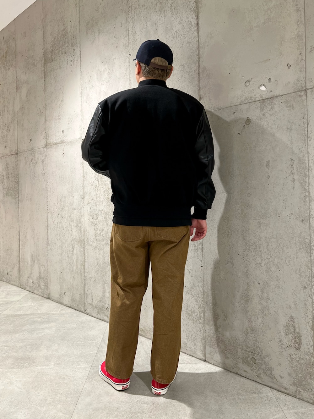 ブラック系のスタジャン、レッド系のスニーカー、ブラウン系のデニムパンツを着用したメンズの秋コーディネートの3枚目の写真