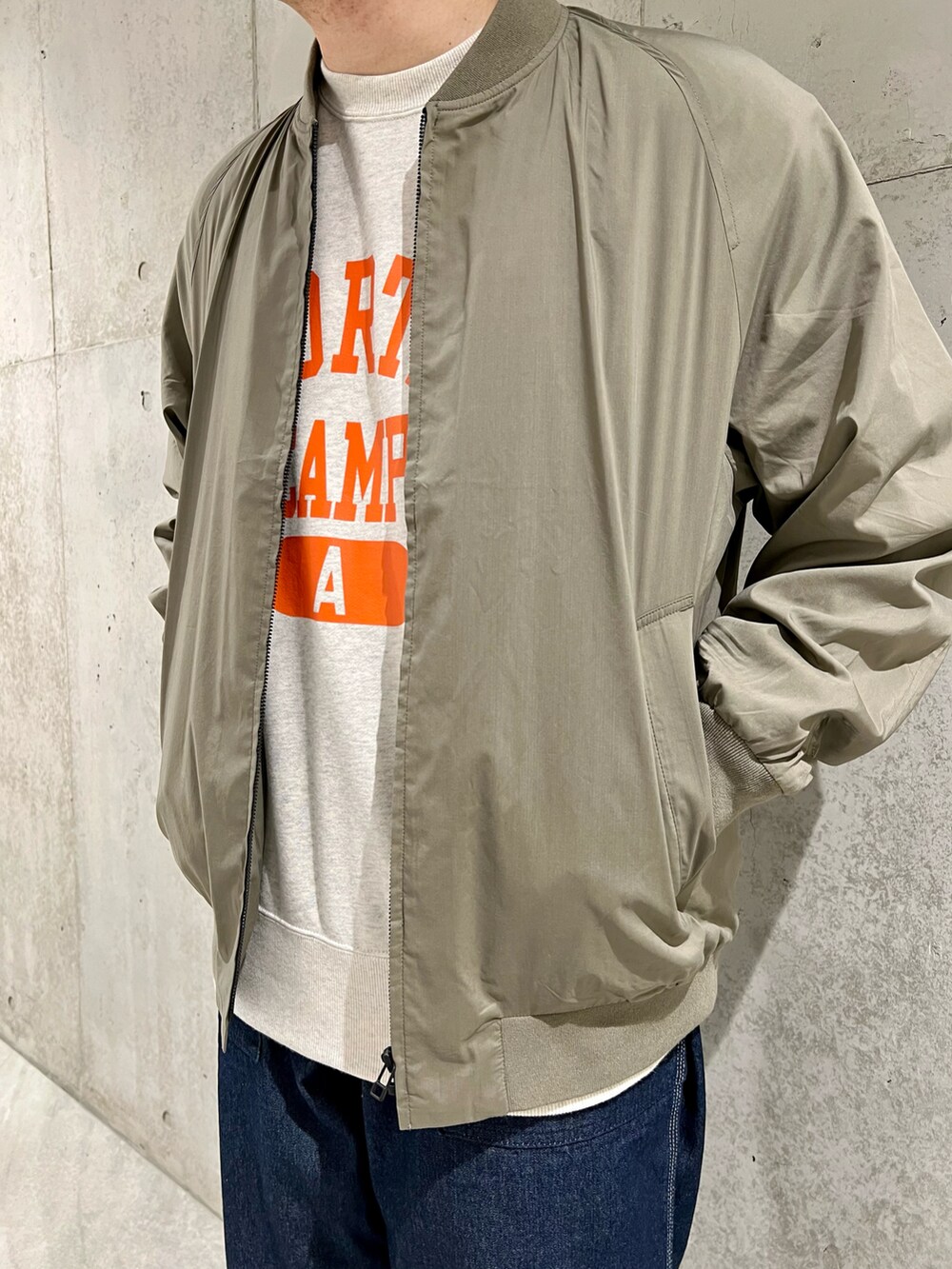 グリーン系のブルゾン、ベージュ系のTシャツ/カットソー、ブルー系のデニムパンツを着用したメンズの春コーディネートの2枚目の写真