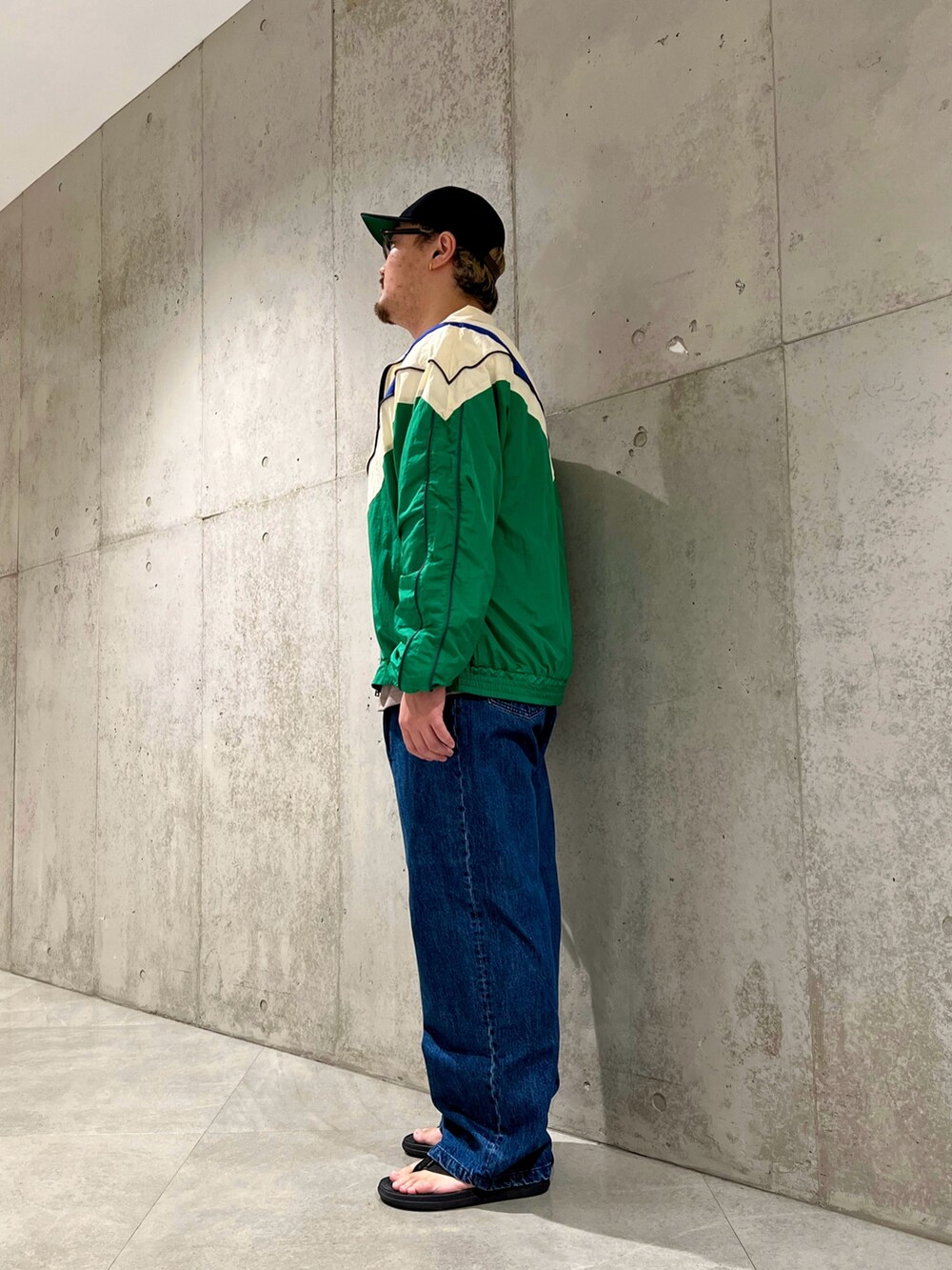 グリーン系のナイロンジャケット、ベージュ系のTシャツ/カットソー、ブルー系のデニムパンツを着用したメンズの夏コーディネートの2枚目の写真