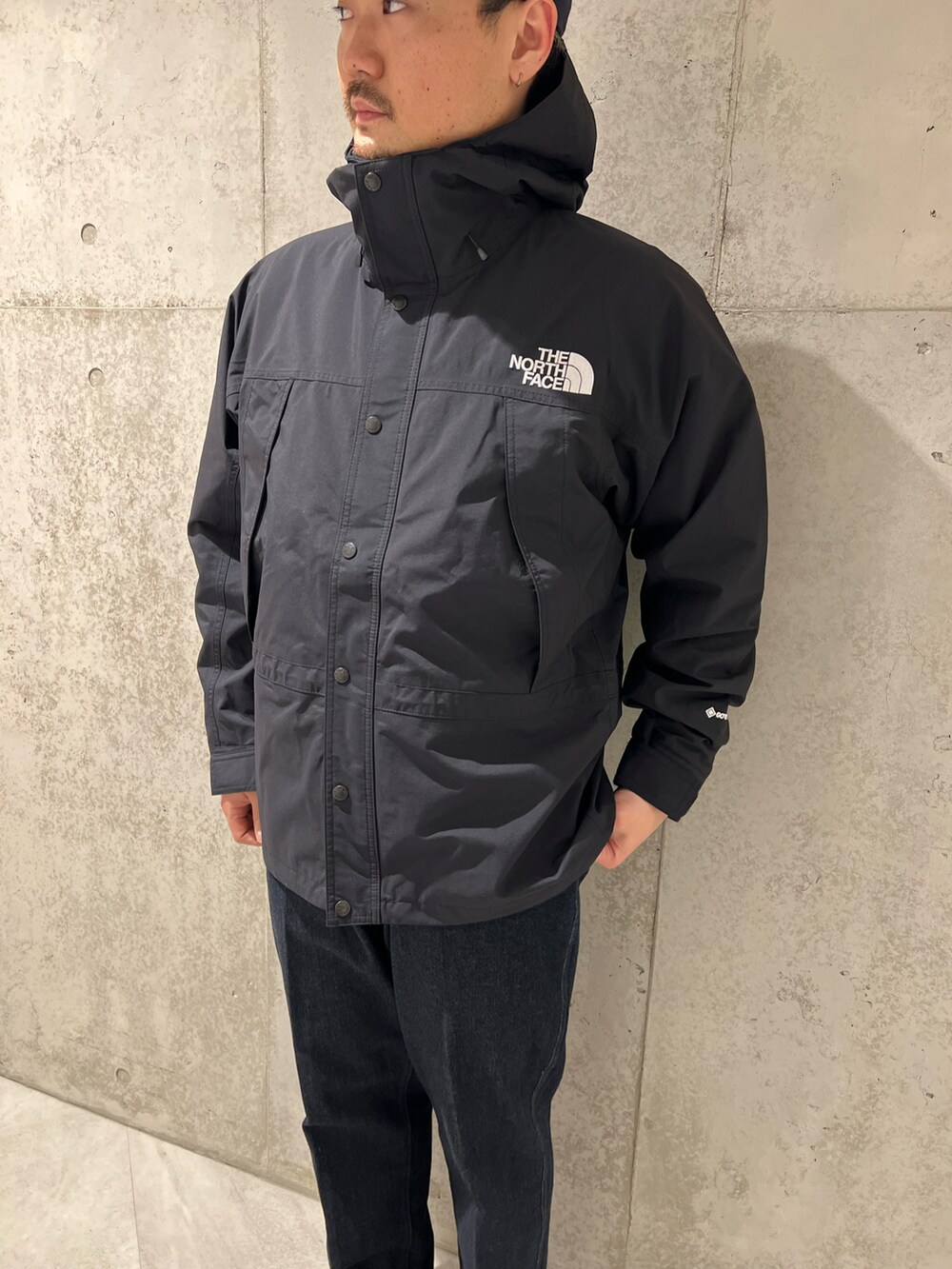 ブラック系のナイロンジャケット、ブルー系のデニムパンツ、ブラック系のブーツを着用したメンズの春コーディネートの2枚目の写真