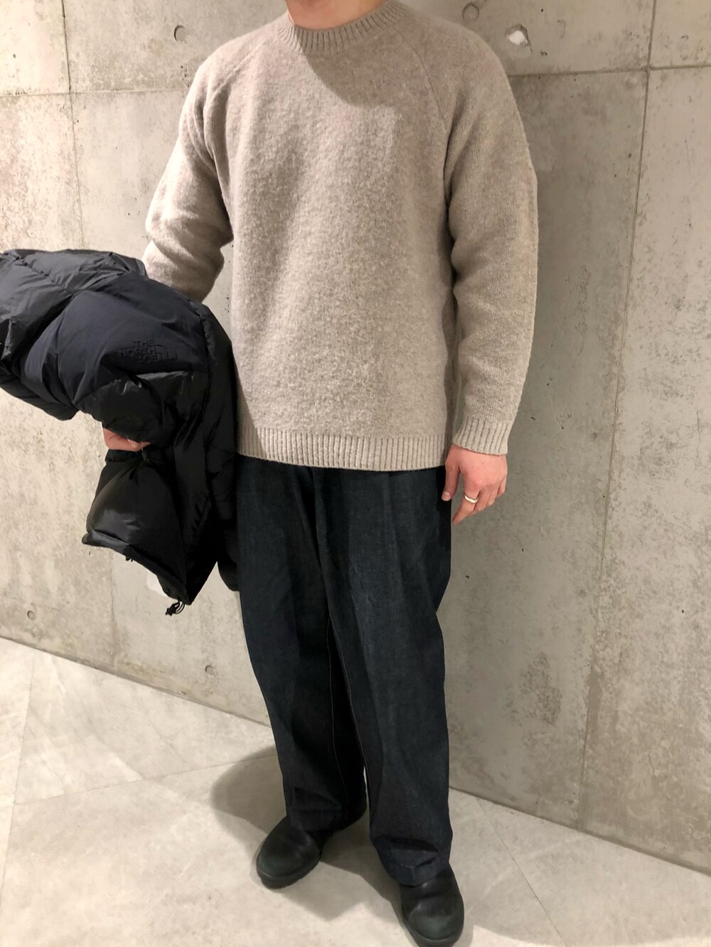 ブラック系のダウンジャケット/コート、ベージュ系のニット/セーター、ブルー系のデニムパンツを着用したメンズの冬コーディネートの4枚目の写真