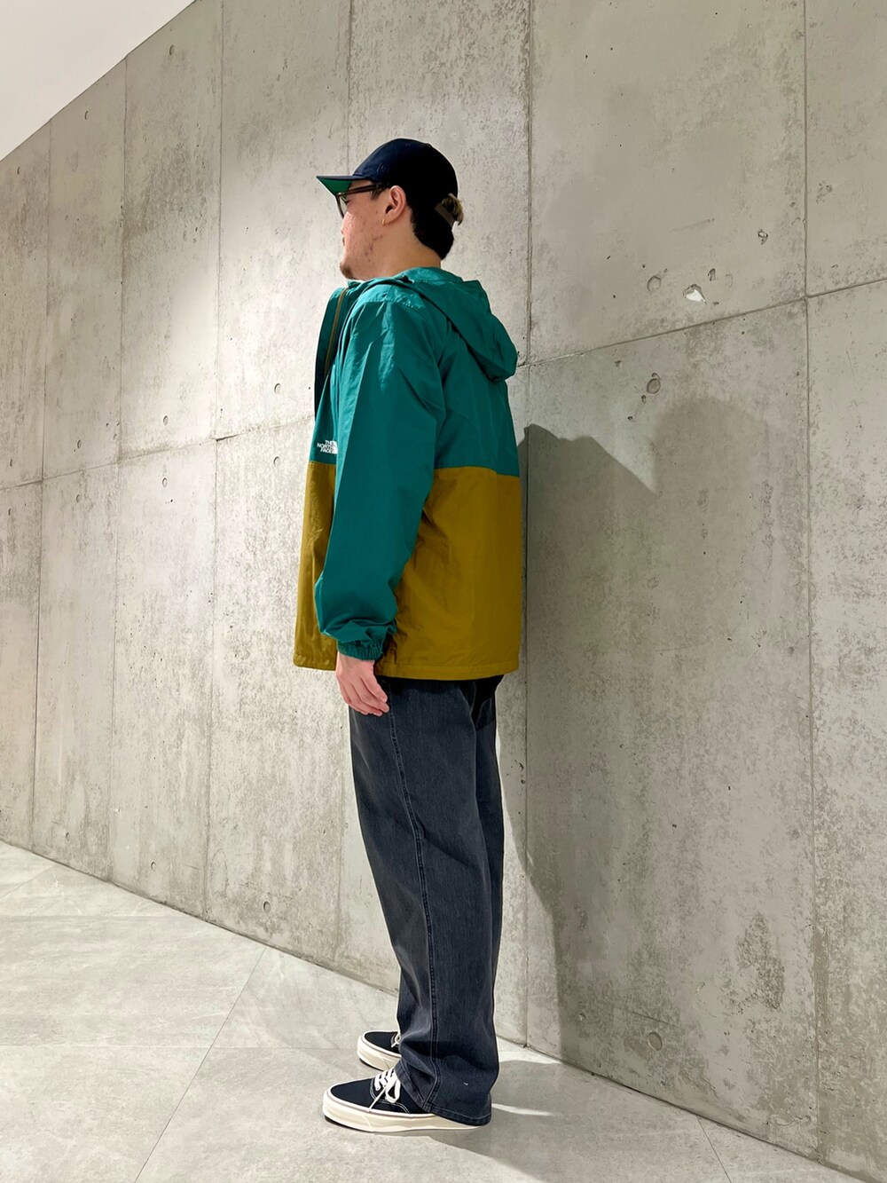 グリーン系のナイロンジャケット、ブラック系のデニムパンツ、ブラック系のスニーカーを着用したメンズの秋コーディネートの2枚目の写真