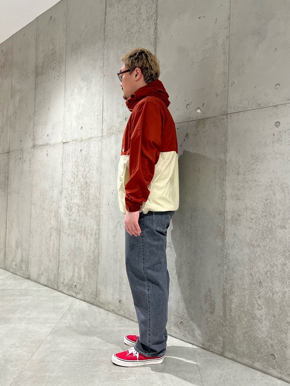 レッド系のナイロンジャケット、ブラック系のデニムパンツ、レッド系のスニーカーを着用したメンズの春コーディネートの2枚目の写真